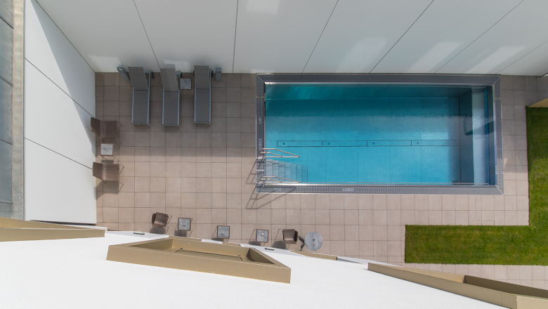 Pohled na bazén zvenčí, © Klinglhuber Pohled shora na obdélníkový bazén s lehátky a stolky na vykachlíkované terase.