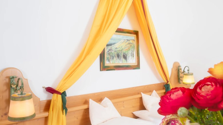 Double room, © Hotel VinoQ A cozy double room with a yellow canopy, wooden bed, wall lamps and a bouquet of flowers in the foreground.