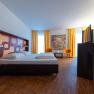 arte Hotel Krems, © Niederösterreich Werbung / Maximilian Pawlikowsky Modernes Hotelzimmer mit Doppelbett, buntem Wandmuster, zwei orangefarbenen Stühlen und gelben Vorhängen.
