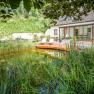 Schwimmbiotop und Garten, © Familie Hofbauer Ein Haus mit Terrasse und Schwimmbiotop im Garten, umgeben von üppiger Vegetation.