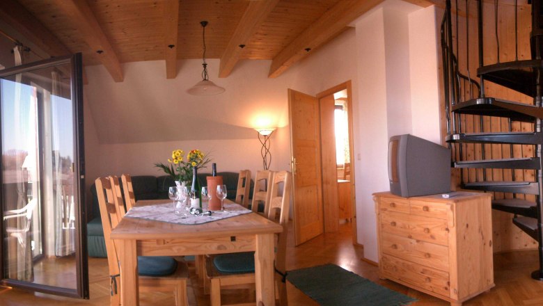 Ploché, © Gartner Clemens Obývací pokoj s dřevěným nábytkem, jídelním stolem, točitým schodištěm a balkonem.