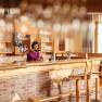 Wein.Restaurant Neustifter, © Weinviertel Tourismus / Michael Reidinger Eine Frau steht hinter einer Bar in einem rustikalen Restaurant und schenkt Wein ein.
