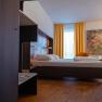 arte Hotel Krems, © Niederösterreich Werbung / Maximilian Pawlikowsky Modernes Hotelzimmer mit Bett, gelben Vorhängen und buntem Gemälde an der Wand.