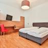 Hotel Unter den Linden Zimmer 103, © Hotel Unter den Linden Hotelzimmer mit Doppelbett, rotem Stuhl, Schreibtisch und Fernseher.