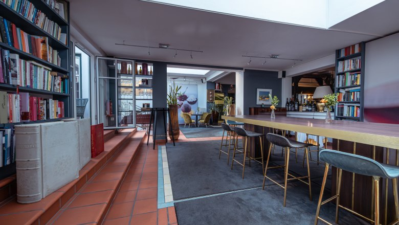 Relais & Chateaux MÖRWALD Hotel am Wagram, © Niederösterreich Werbung / Maximilian Pawlikowsky Pohled do interiéru moderního hotelového pokoje s policemi na knihy, vysokými stoly a barovými židlemi.