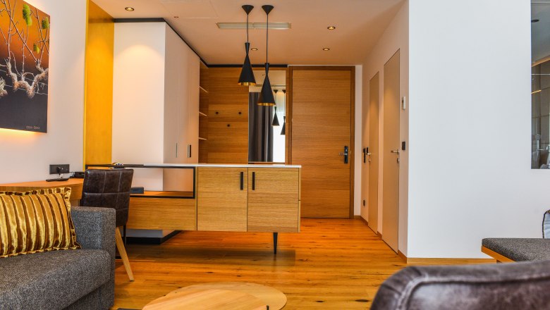 Suite Hotel Klinglhuber, © Franz Klinglhuber GmbH Pohled do interiéru moderního hotelového apartmá s dřevěnou podlahou, šedou pohovkou a dřevěným psacím stolem.