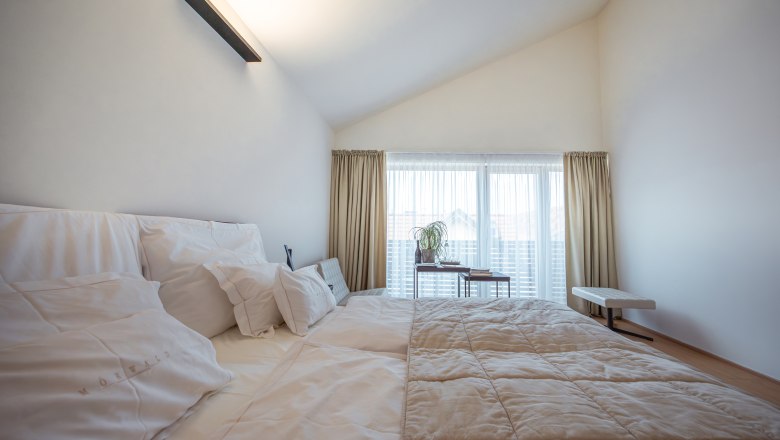 Relais & Chateaux Mörwald Hotel am Wagram, © Niederösterreich Werbung / Maximilian Pawlikowsky Modernes Hotelzimmer mit großem Bett, weißen Kissen und Tagesdecke, helle Vorhänge und Fenster im Hintergrund.