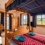 Zimmer Nr. 3 Himmelbett, © Weingut Zöhrer Ein gemütliches Zimmer mit Himmelbett, Holzmöbeln und Blick auf Weinberge. Eine Weinflasche ist im Vordergrund abgebildet.