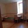 Gästezimmer, © Geistliches Jugendzentrum Oberleis Ein einfach eingerichtetes Gästezimmer mit Holzboden, Einzelbett, Etagenbett, Tisch und Stühlen, sowie einem Fenster mit Vorhang.