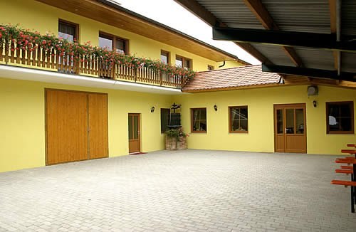 Vnitřní nádvoří, © Berg-Hahn Vnitřní dvůr žluté budovy s dřevěnými dveřmi a balkonem s květinami.