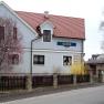 Haus, © Waltner Ein zweistöckiges Haus mit rotem Dach und blauer Fassade, umgeben von blühenden Bäumen und einem Holzzaun.