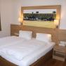 Gästezimmer, © Familie Rieder Ein Gästezimmer mit einem Doppelbett, Holzverkleidung, Nachttisch und einem Bild von Weinbergen an der Wand.