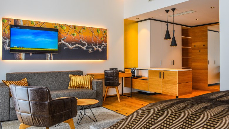 Příklad apartmá ve společnosti Klinglhuber, © Franz Klinglhuber GmbH Moderní hotelové apartmá s pohovkou, křeslem, TV a kuchyňským koutem.