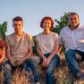 Familie Berger, © Weingut und Gästehaus Berger Vier Personen sitzen auf einem Feld im Sonnenuntergang.