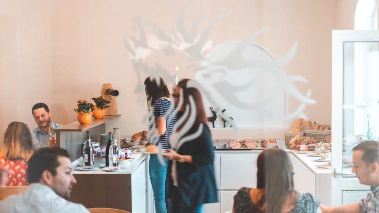 Snídaně formou bufetu, © Matthias Auer V jasně osvětlené místnosti si lidé podávají snídani formou bufetu.