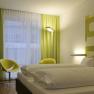 arte Hotel, © arte Hotel Modernes Hotelzimmer mit Doppelbett, grün-gelben Vorhängen und Wanddekor.