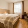 Hotel Unter den Linden Zimmer 215, © Hotel Unter den Linden Hotelzimmer mit Doppelbett, Schreibtisch und Fenster mit Vorhängen.