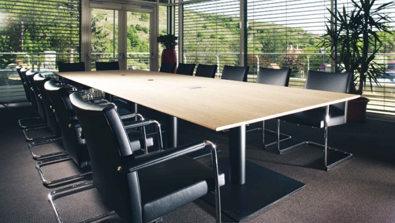 Steigenberger Krems, Seminarraum Spitz, © Steigenberger Hotel and Spa, Andreas Hofer Moderner Seminarraum mit großem Holztisch und schwarzen Stühlen, umgeben von Glaswänden mit Blick auf grüne Landschaft.