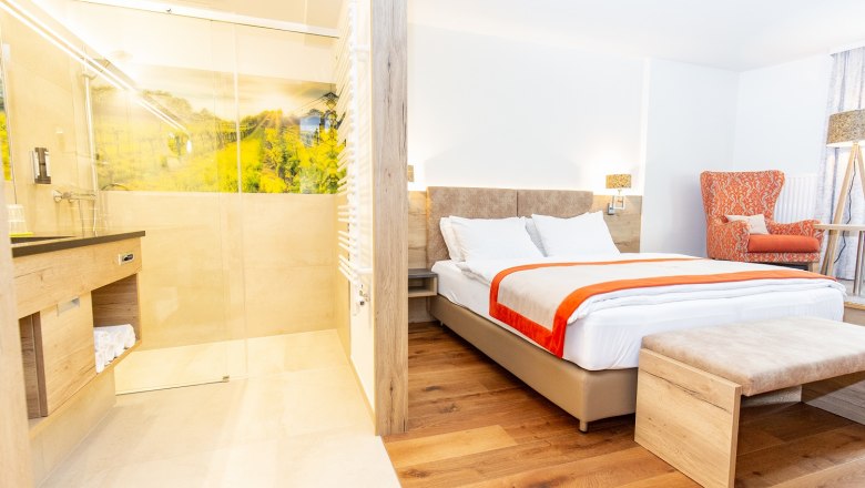 TDR-Hopfeld Dreikönigshof-Genuss.Zimmer, © flotographix -Kampl Florian Modern hotel room with double bed, orange armchair and open shower.