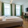 Hotel Unter den Linden 206, © Hotel Unter den Linden Hotelzimmer mit Doppelbett, grüne Vorhänge, Schreibtisch, Stuhl und Wand-TV.