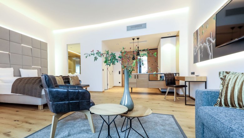 Venkovní výhled na bazén z vrcholu, © Klinglhuber Moderně zařízený hotelový pokoj s postelí, křesly, stolem a dekoracemi.