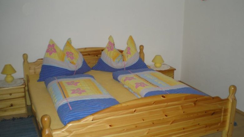 Holzbett mit bunter Bettw&auml;sche in einem Schlafzimmer.
