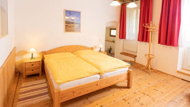 Gem&uuml;tliches Schlafzimmer mit Holzm&ouml;beln, gelber Bettw&auml;sche und roten Vorh&auml;ngen.