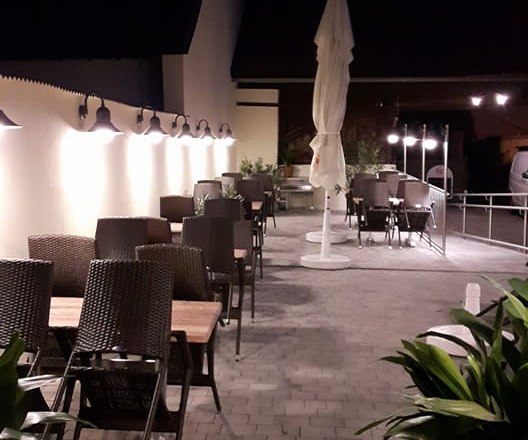 Ein leerer Gastgarten bei Nacht mit Tischen, Stühlen und Pflanzen.