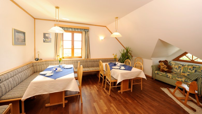 &Uacute;tuln&yacute; sn&iacute;daňov&yacute; koutek s dřevěn&yacute;m n&aacute;bytkem, prostřen&yacute;mi stoly a pohovkou s ply&scaron;ov&yacute;mi medv&iacute;dky.