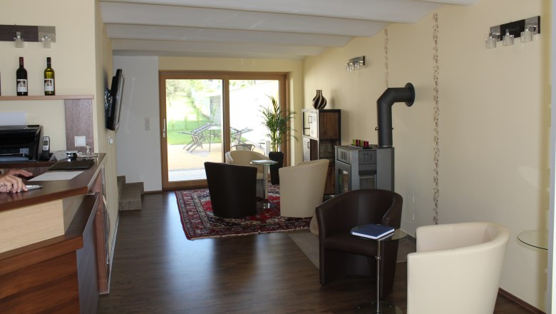 Innenansicht eines modernen G&auml;stehauses mit Sitzbereich, Kamin und Glast&uuml;r zum Garten.