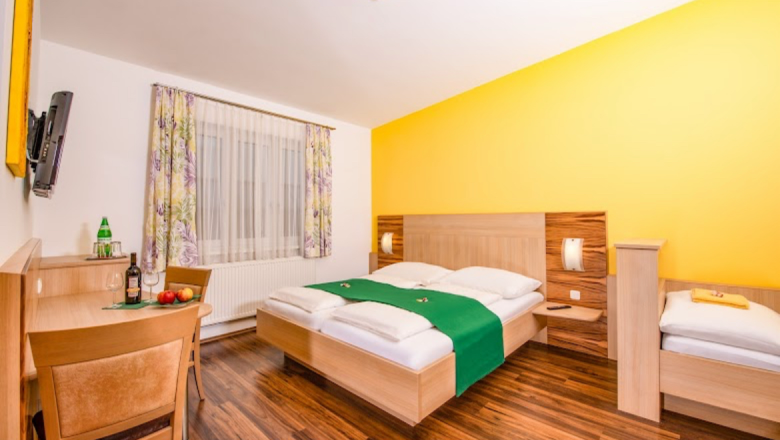 Zimmerbeispiel im Winzerhof Steinbatz, © Familie Steinbatz Doppelbett in einem Raum mit dunklem Fußboden und gelber Rückwand