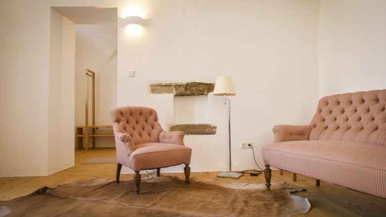 A cozy living room with an armchair, a sofa, a floor lamp and a carpet on a wooden floor.
