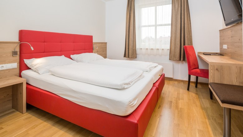 Modernes Hotelzimmer mit rotem Bett und Schreibtisch.
