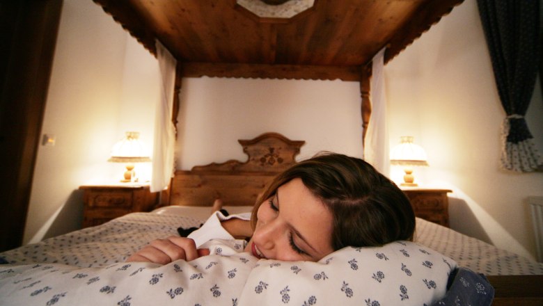 Woman lying smiling on a bed in a cozy hotel room with wooden decor.