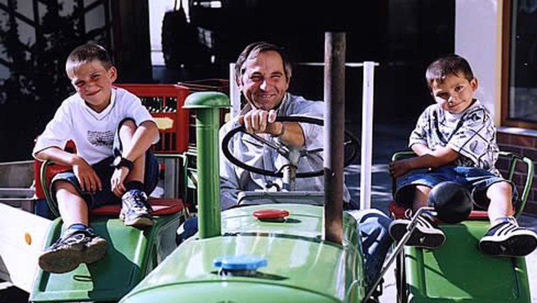 Ein Mann und zwei Kinder sitzen auf einem grünen Traktor.
