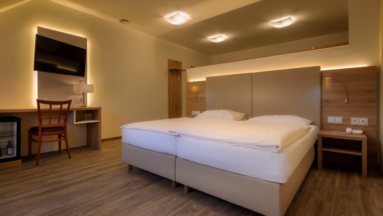 Modernes Hotelzimmer mit Doppelbett, Schreibtisch, Stuhl und Fernseher.
