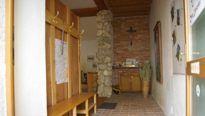 Eingangsbereich mit Holzb&auml;nken, Steinwand und Kreuz.