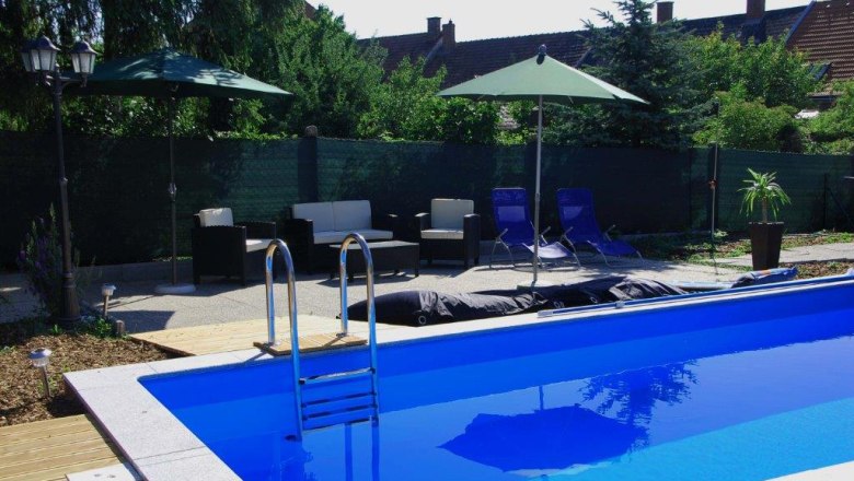 Ein Außenbereich mit einem blauen Pool, umgeben von Liegestühlen, Sonnenschirmen und Gartenmöbeln.