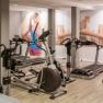 Fitnessraum mit Laufbändern und Fitnessgeräten, Wandbild einer Frau beim Laufen.