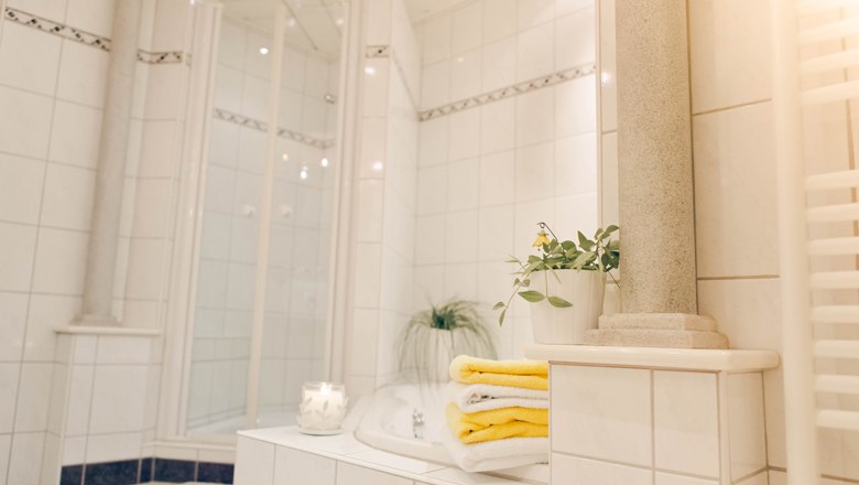 Modern bathroom with white tiles, yellow towels and plants.