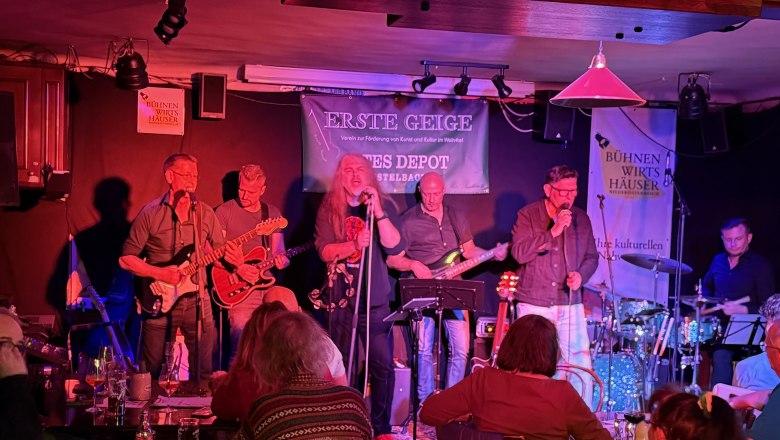 Band spielt auf einer B&uuml;hne in einem kleinen Veranstaltungsort mit Publikum.