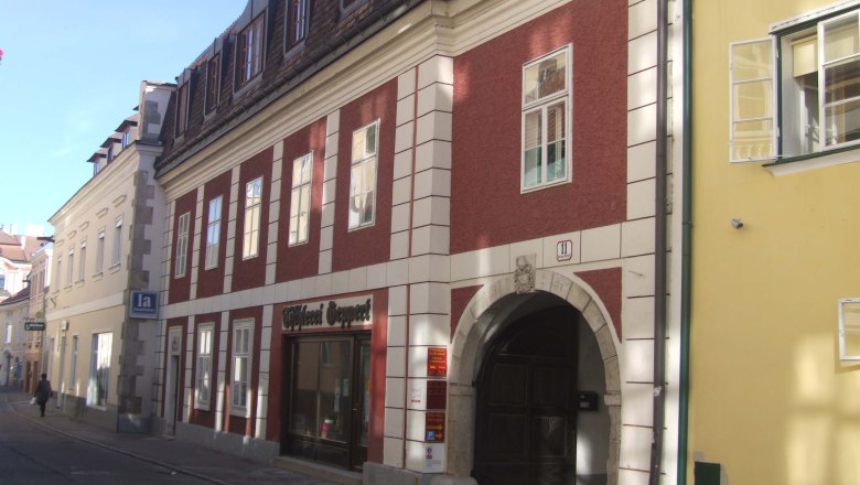 Historisches Gebäude mit roter Fassade und Torbogen in einer Straße.