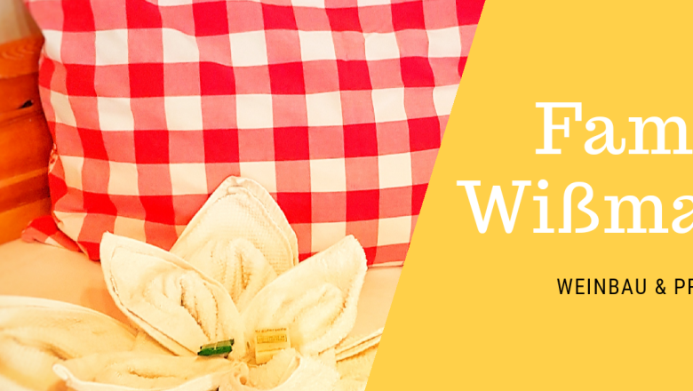 Červen&yacute; pol&scaron;t&aacute;ř s kostkovan&yacute;m vzorem a ručn&iacute;k ve tvaru květiny na posteli. Text: Wi&szlig;mann, vinařstv&iacute; a soukrom&eacute; pokoje.