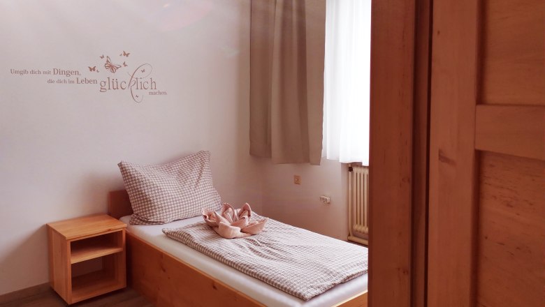 Ein einfaches G&auml;stezimmer mit einem Einzelbett, Holzregal und einem Zitat an der Wand.