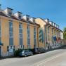 Außenansicht eines gelb-blauen Hotels mit mehreren Fenstern und geparkten Autos davor.