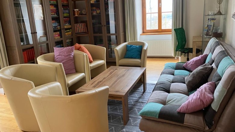 Ein gemütlicher Gemeinschaftsraum mit Sesseln, einem Sofa, einem Tisch und Bücherregalen.
