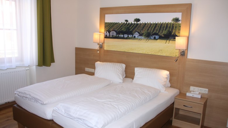 A guest room with a double bed, wooden paneling, bedside table and a picture of vineyards on the wall.