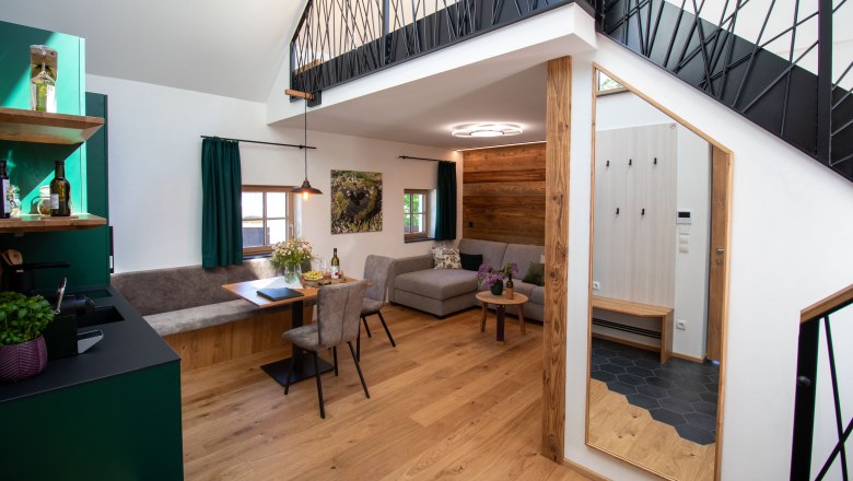 Modern&iacute; byt s dřevěnou podlahou, &scaron;edou pohovkou, j&iacute;deln&iacute;m stolem a otevřenou galeri&iacute;.