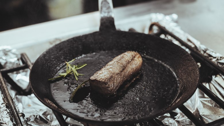 A piece of meat roasts in a cast-iron pan with rosemary.