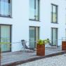Moderne Terrasse mit Liegestühlen und Pflanzen vor einem Gebäude mit großen Fenstern.